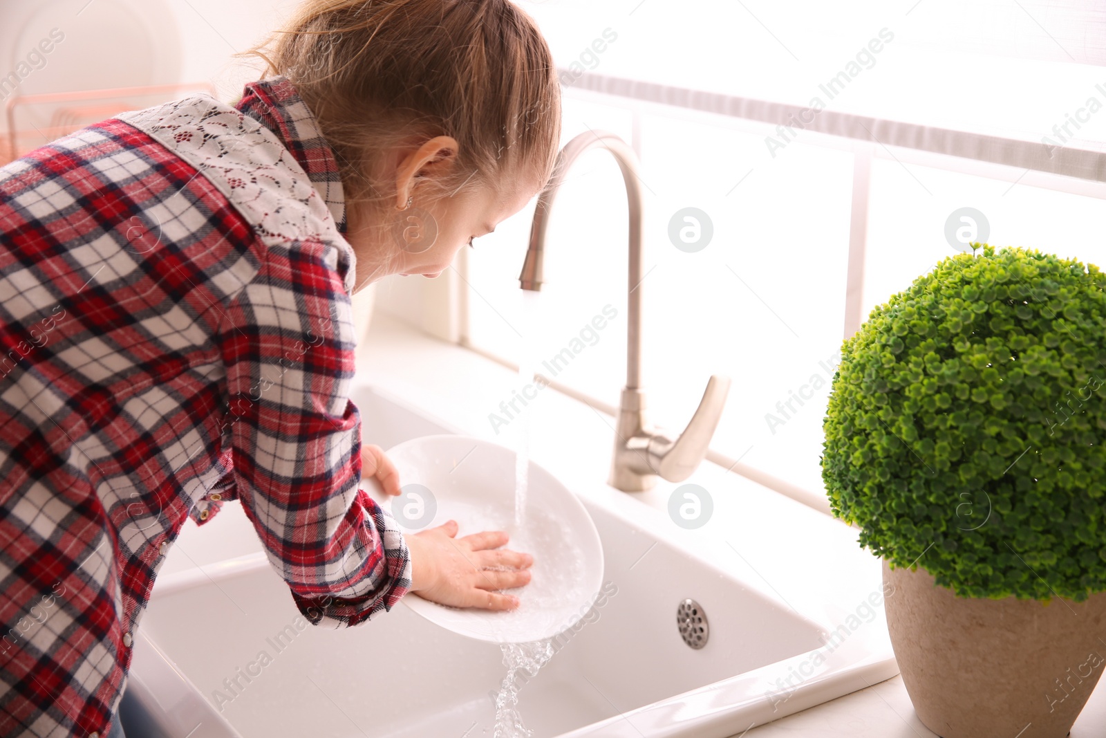 Photo of Little girl washing dishes in kitchen at home