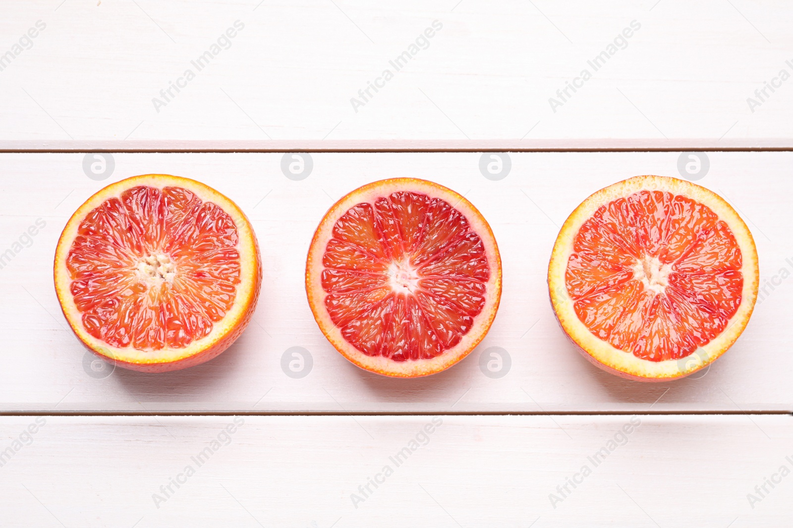 Photo of Halves of ripe red oranges on white wooden table, flat lay
