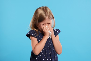 Photo of Suffering from allergy. Little girl with tissue sneezing on light blue background