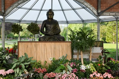Photo of Golden Buddha sculpture surrounded by beautiful potted plants on wooden pedestal indoors