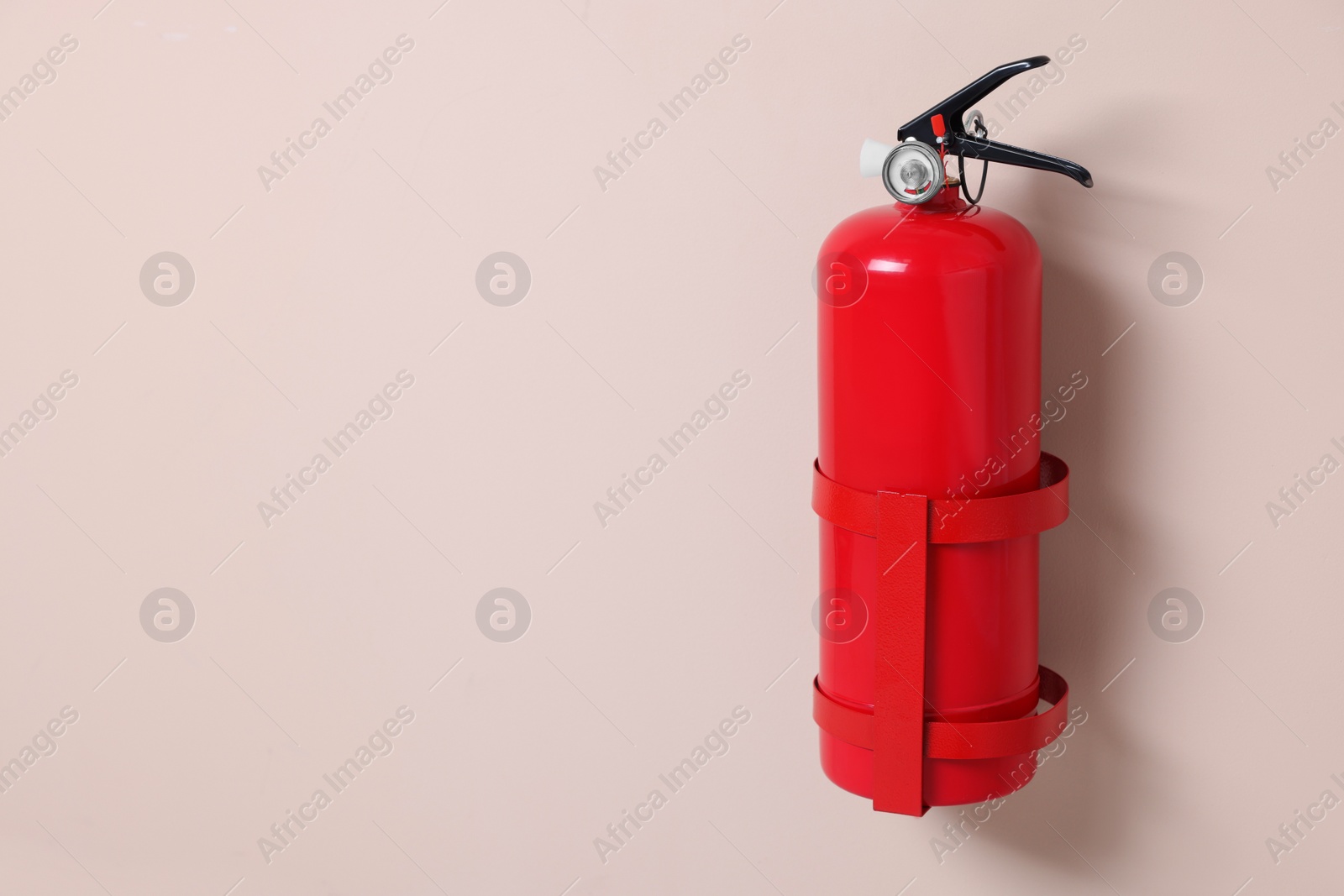 Photo of One fire extinguisher on beige wall, space for text