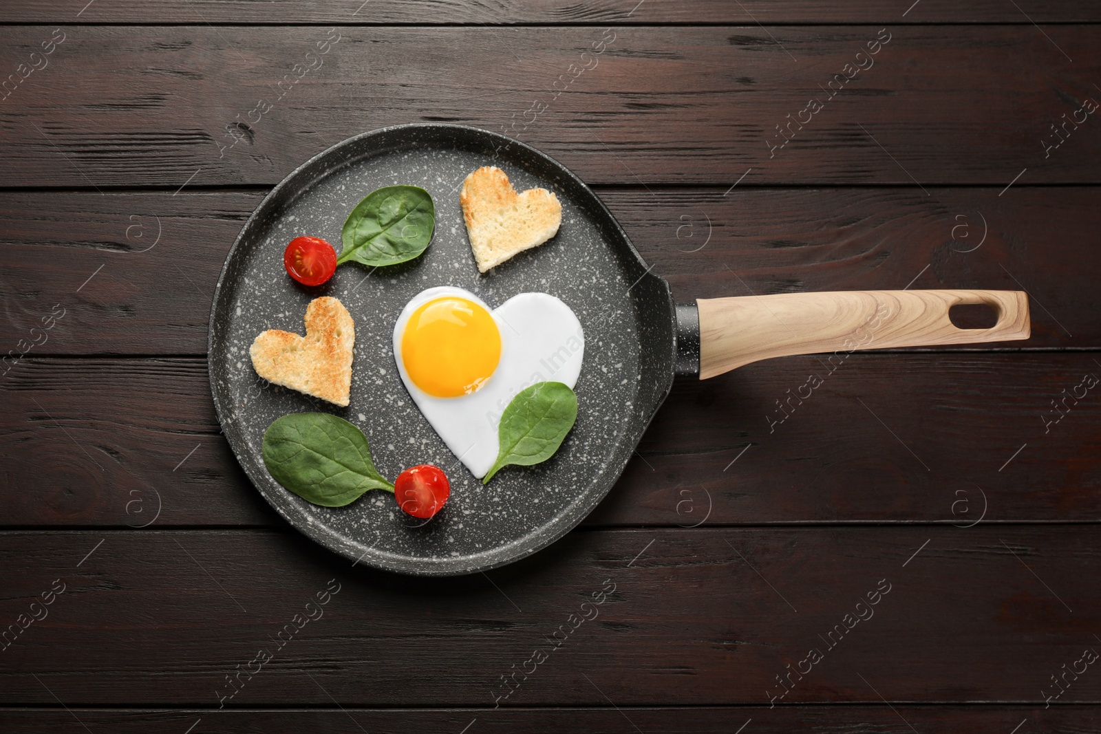 Photo of Romantic breakfast with heart shaped fried egg, toasts, spinach and tomatoes in pan on wooden table, top view