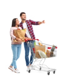 Young couple with full shopping cart and paper bags on white background