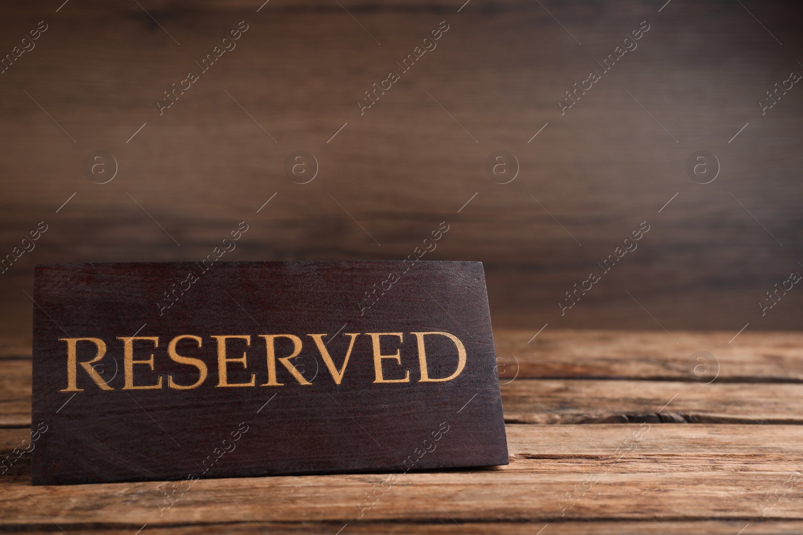 Photo of Elegant sign RESERVED on wooden surface, space for text. Table setting element