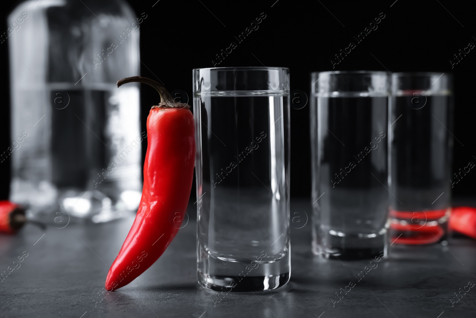 Photo of Red hot chili peppers and vodka on grey table against black background