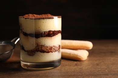 Delicious tiramisu in glass on wooden table, closeup. Space for text