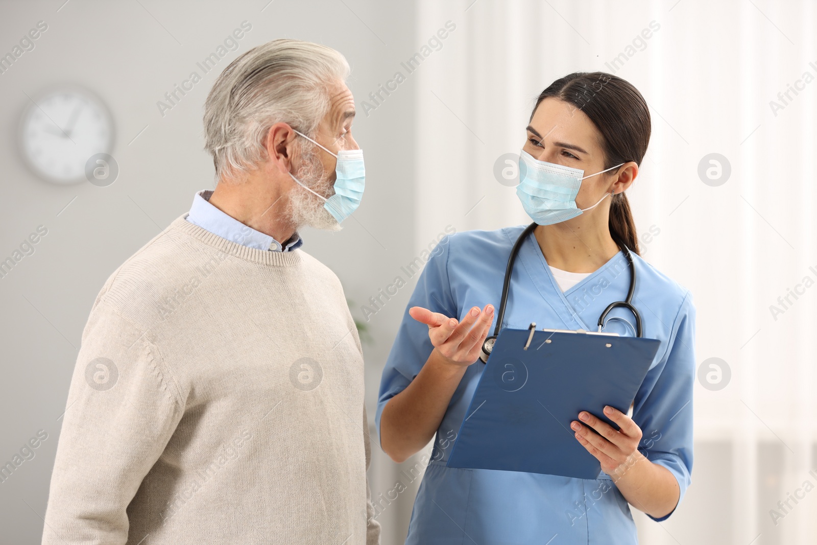 Photo of Nurse with clipboard consulting elderly patient in hospital