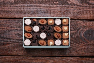 Photo of Box of delicious chocolate candies on wooden table, top view