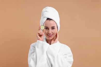 Photo of Beautiful woman in bathrobe with piece of cucumber on beige background