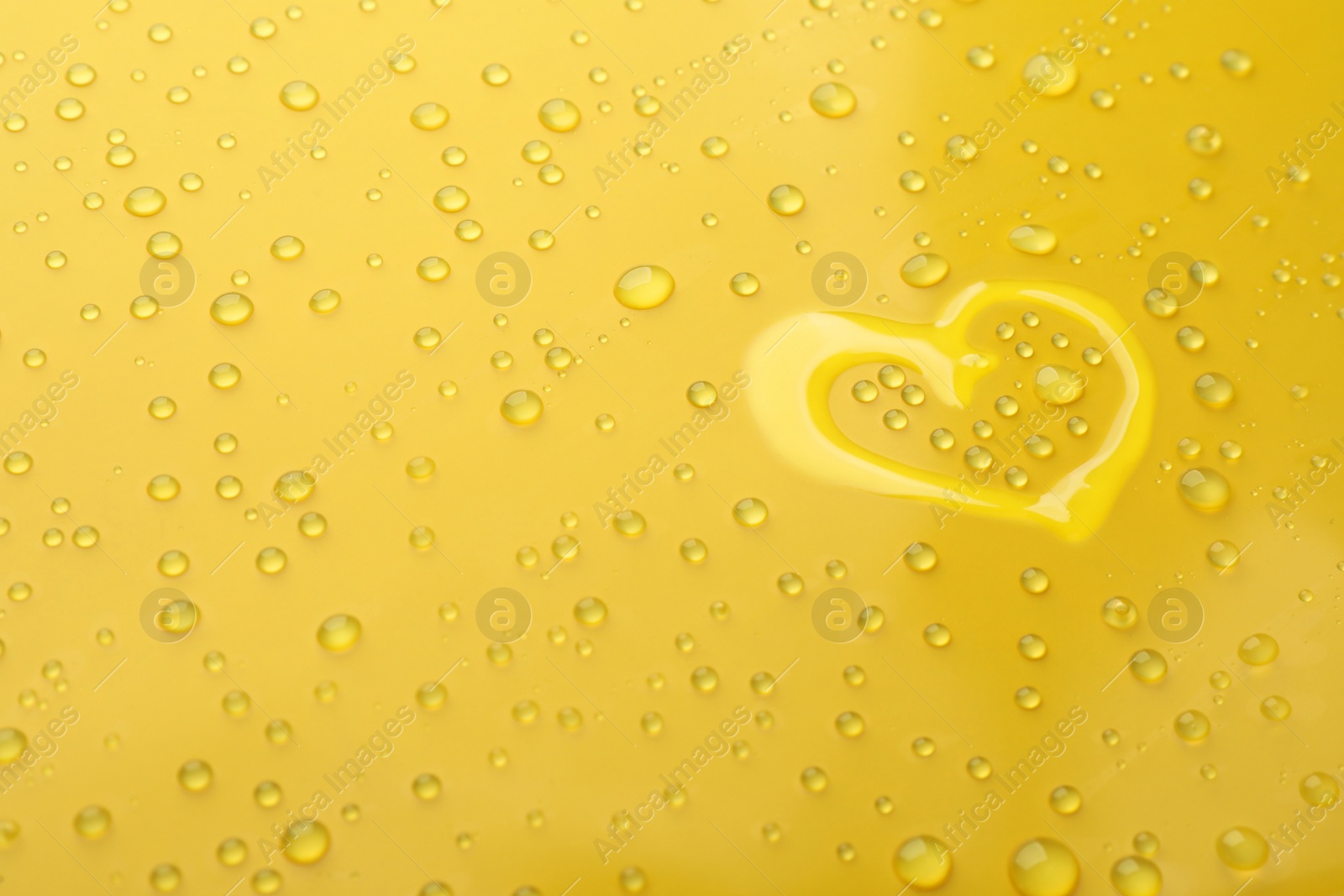 Photo of Heart shape of water and drops on yellow background