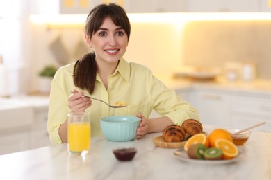 Photo of Smiling woman eating tasty cornflakes at breakfast indoors