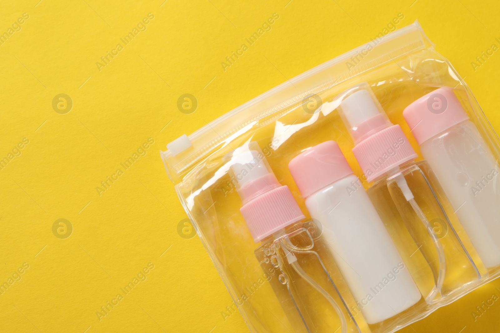 Photo of Cosmetic travel kit in plastic bag on yellow background, top view. Space for text