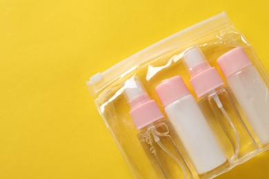 Photo of Cosmetic travel kit in plastic bag on yellow background, top view. Space for text