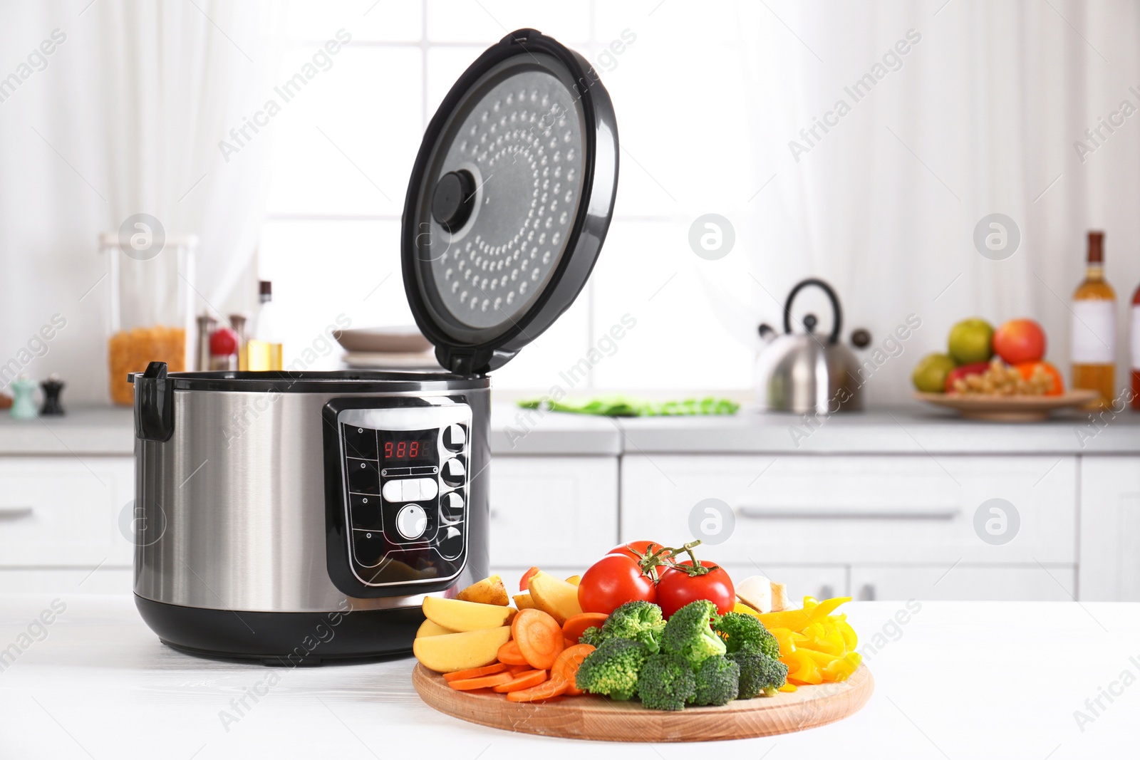 Photo of Modern multi cooker and wooden board with vegetables on white table in kitchen