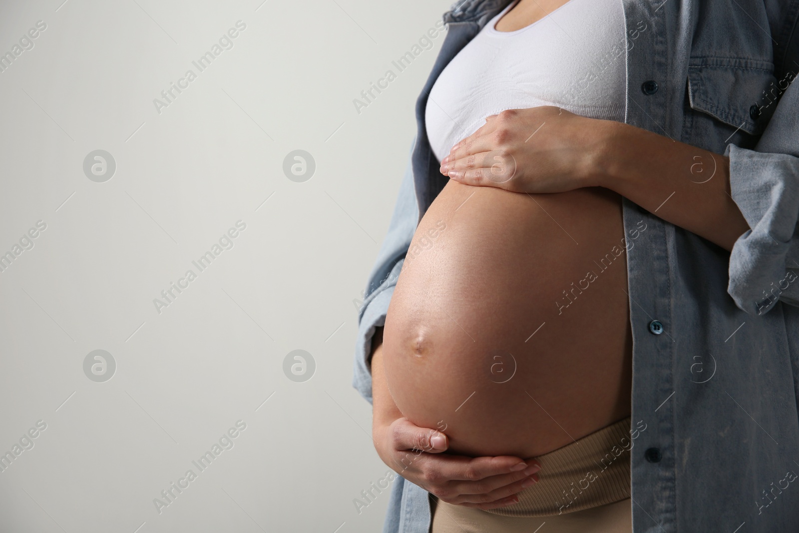 Photo of Pregnant woman touching her belly on light grey background, closeup. Space for text