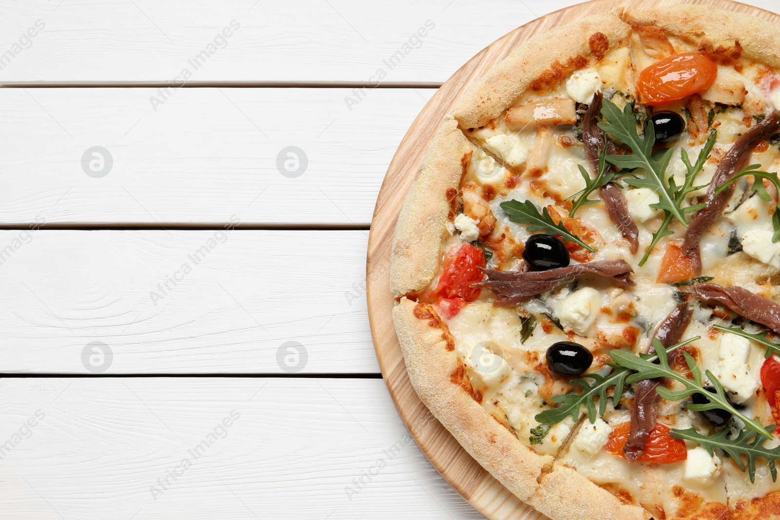 Photo of Tasty pizza with anchovies, arugula and olives on white wooden table, top view. Space for text