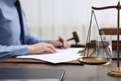 Photo of Lawyer working with documents at wooden table, focus on scales of justice