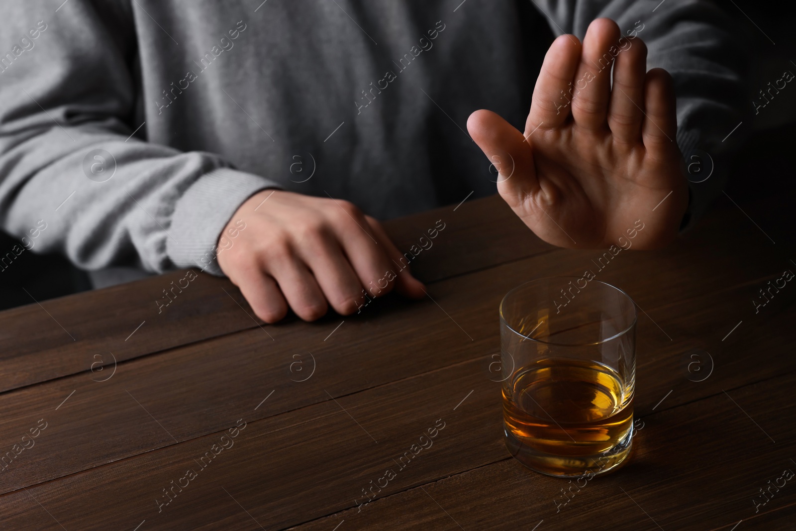 Photo of Man refusing to drink whiskey at wooden table, closeup. Alcohol addiction