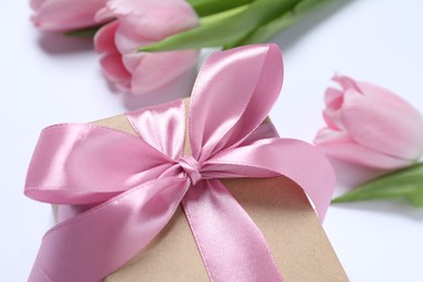 Photo of Beautiful gift box with pink bow and tulips on white background, closeup