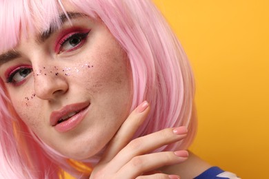 Photo of Beautiful woman with bright makeup and glitter freckles on yellow background, closeup