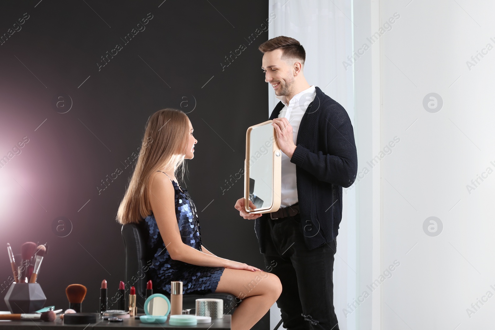 Photo of Professional makeup artist working with beautiful young woman in photo studio