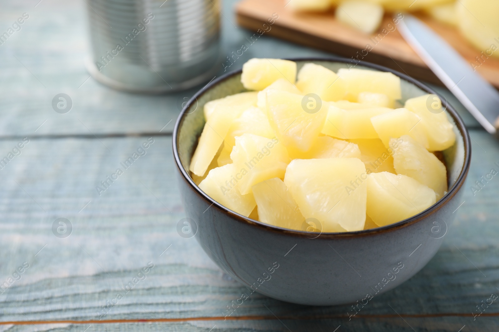 Photo of Pieces of delicious canned pineapple in bowl on light blue wooden table, closeup