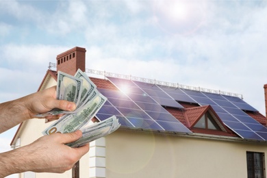 Image of Man counting money against house with installed solar panels. Renewable energy and money saving