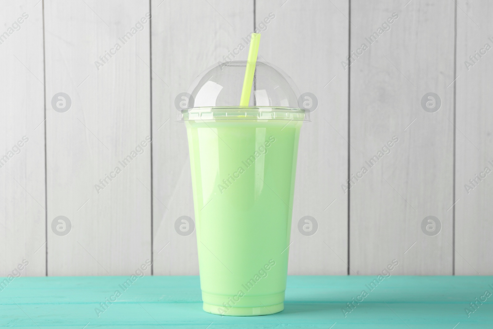 Photo of Tasty smoothie in plastic cup on light blue table against white wooden wall