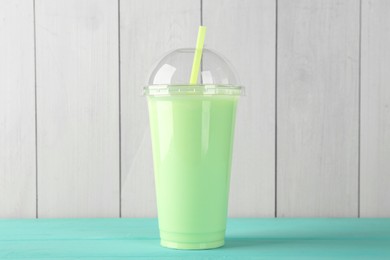 Photo of Tasty smoothie in plastic cup on light blue table against white wooden wall