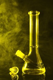 Photo of Glass bong and smoke on black background, toned in yellow. Smoking device