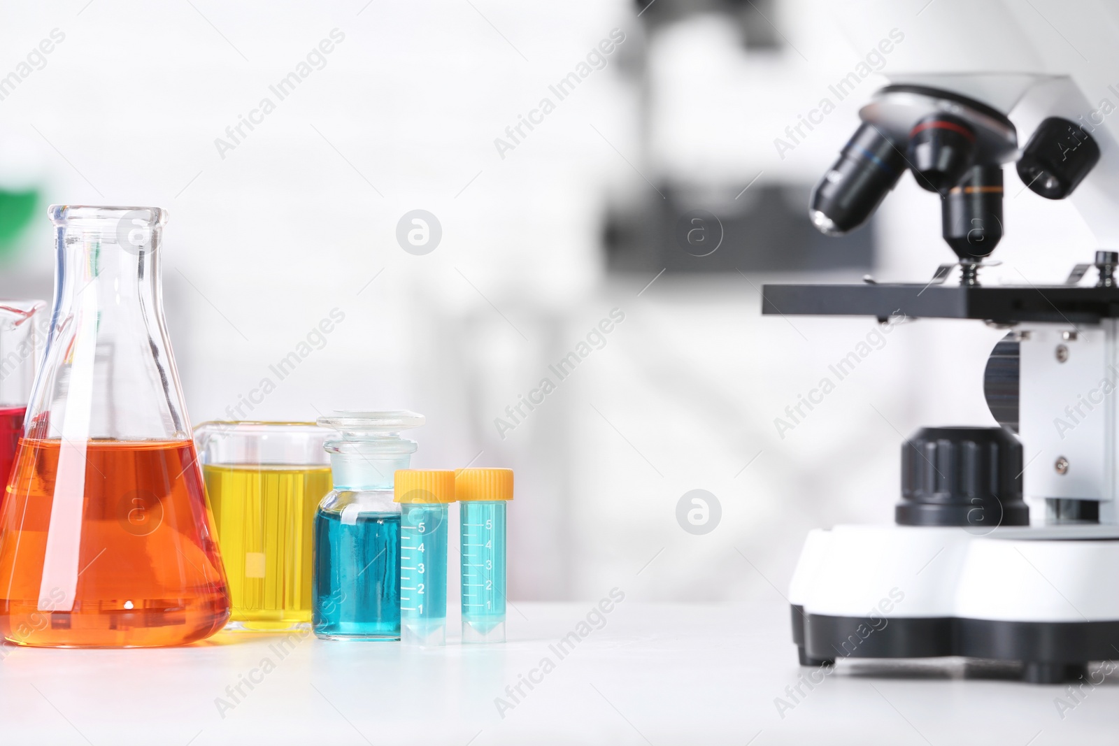 Photo of Different glassware with samples and microscope on table in chemistry laboratory