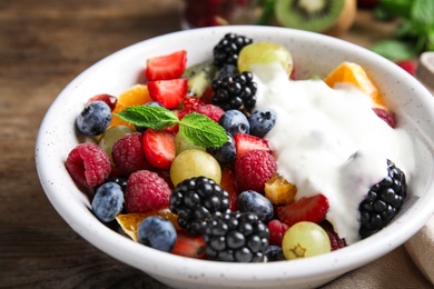 Photo of Fresh tasty fruit salad with yogurt on wooden table, closeup