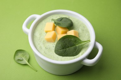 Delicious spinach cream soup with cheese in bowl on green background