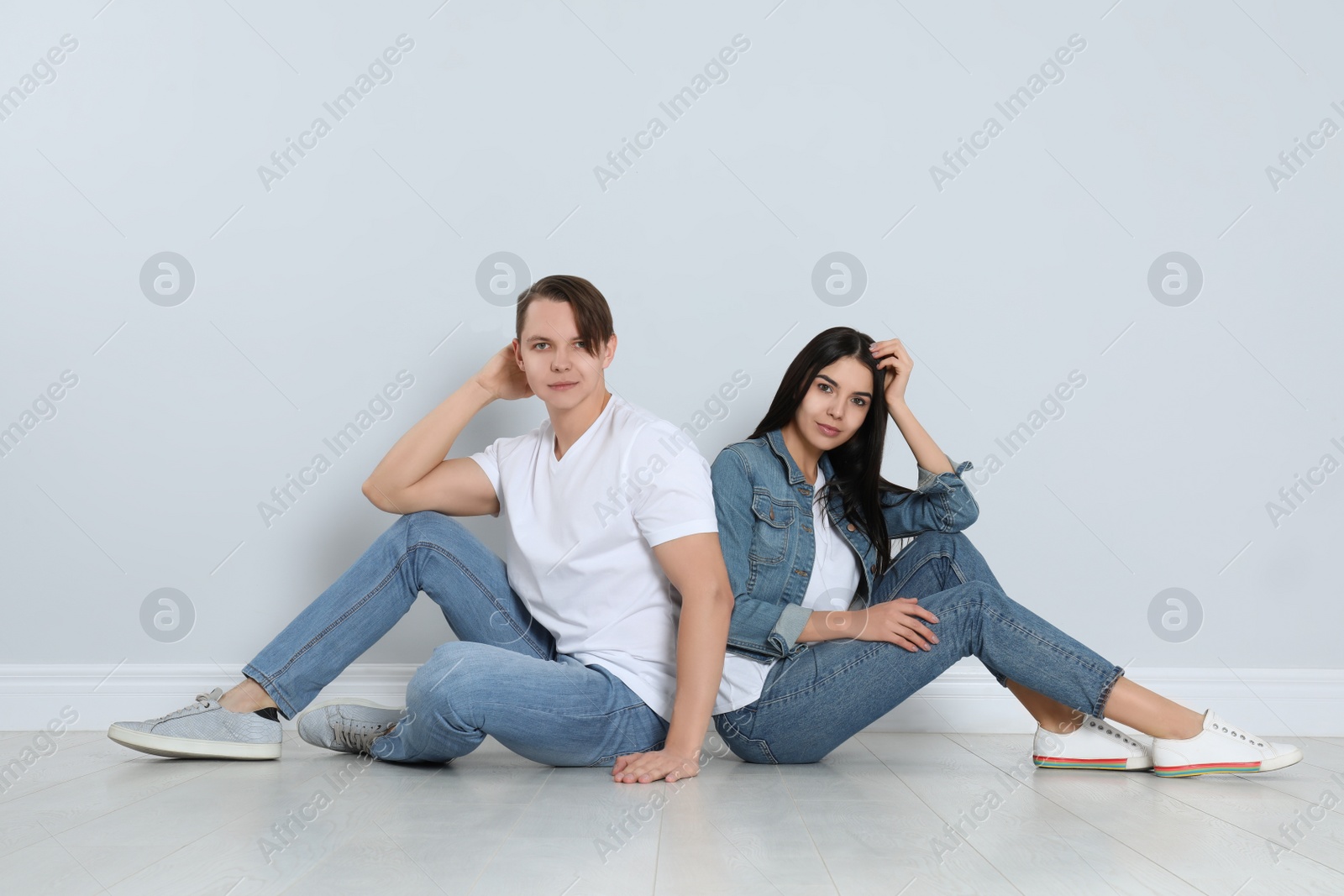 Photo of Young couple in stylish jeans sitting near light wall