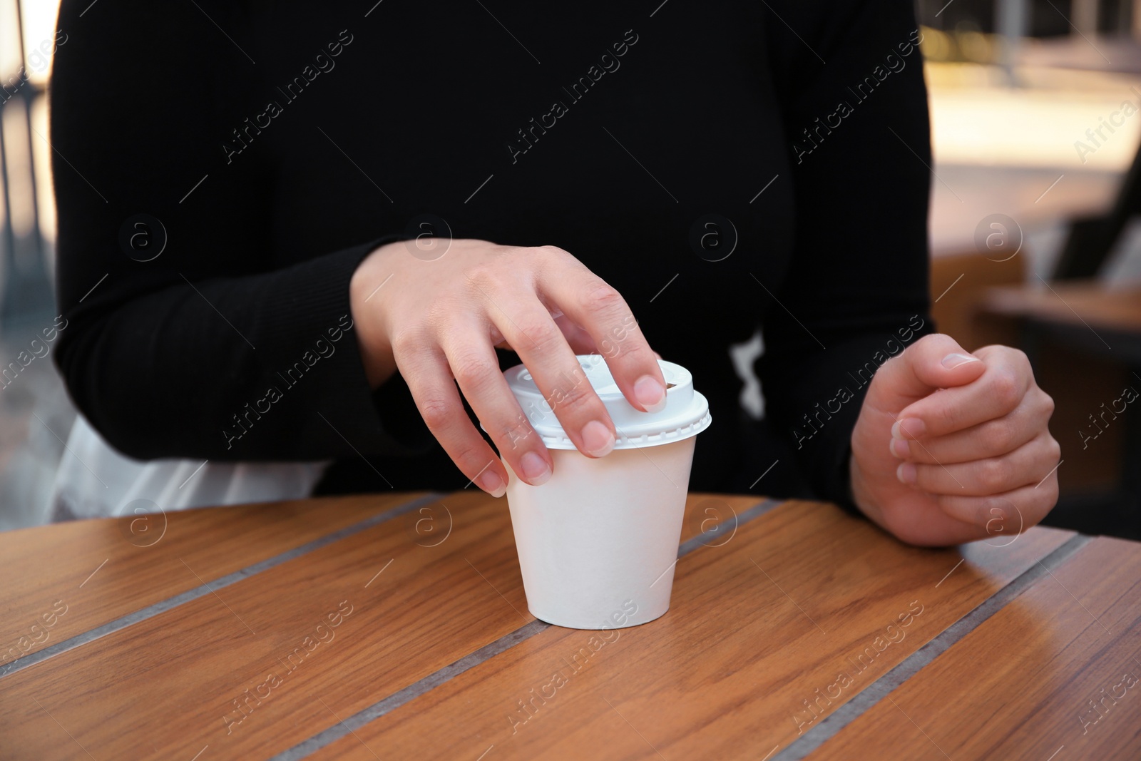 Photo of Woman with cardboard cup of coffee at table outdoors, closeup