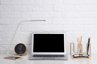 Modern workplace with laptop on table against brick wall. Mockup for design