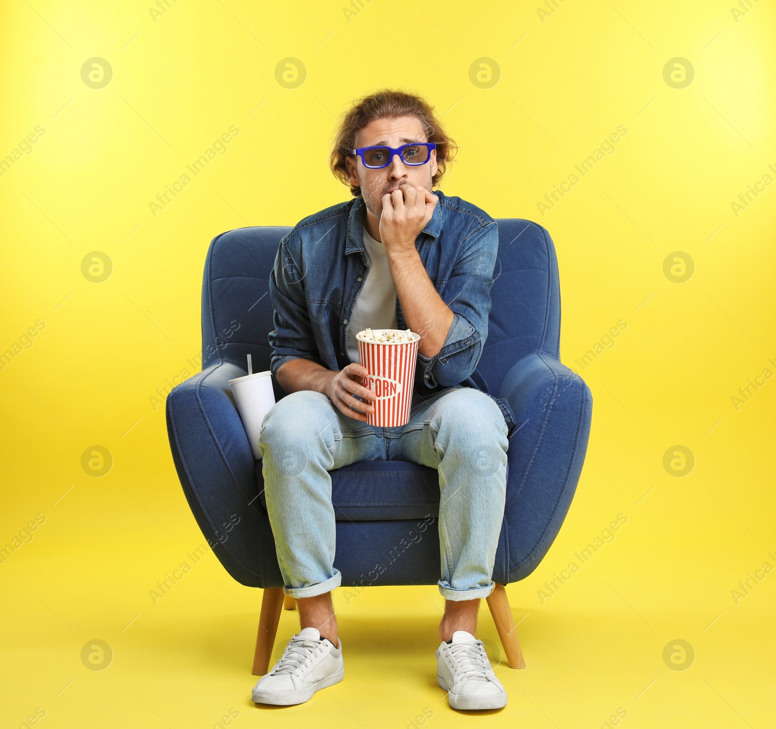 Photo of Emotional man with 3D glasses, popcorn and beverage sitting in armchair during cinema show on color background
