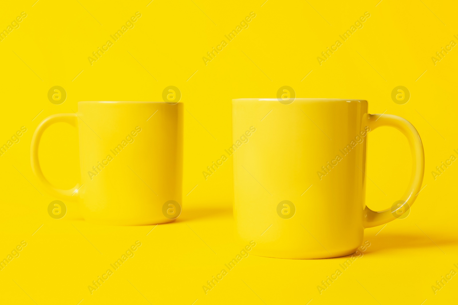 Photo of Two bright ceramic mugs on yellow background