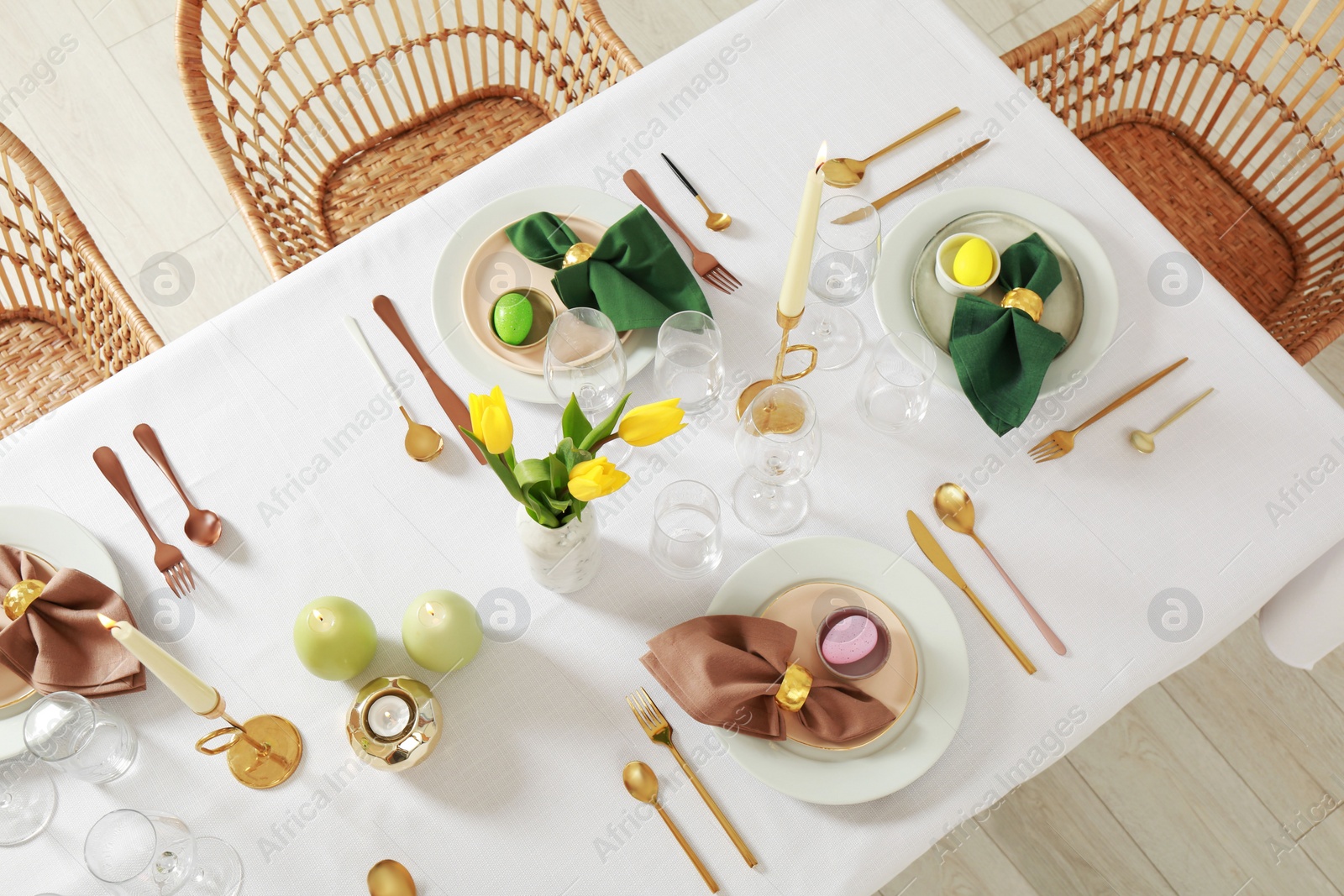 Photo of Festive Easter table setting with painted eggs, burning candles and yellow tulips indoors, view from above