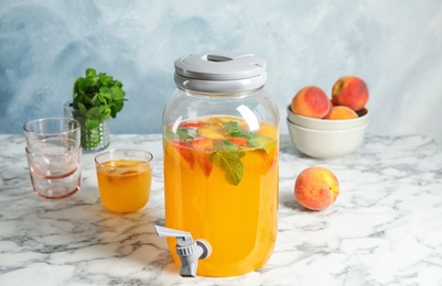 Peach cocktail in glass and jar with tap on table. Refreshing drink