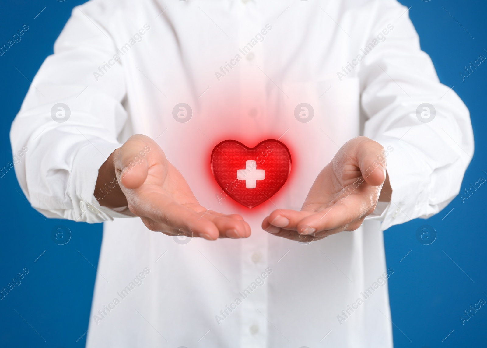 Image of Woman holding red heart in hands on blue background, closeup. Blood donation concept