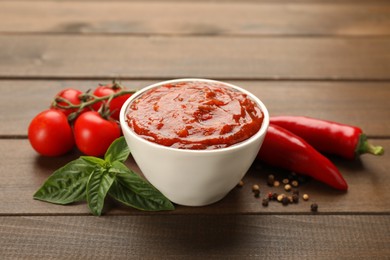 Delicious adjika sauce in bowl and ingredients on wooden table