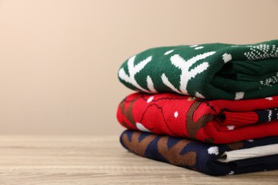 Stack of different Christmas sweaters on wooden table against beige background, closeup. Space for text