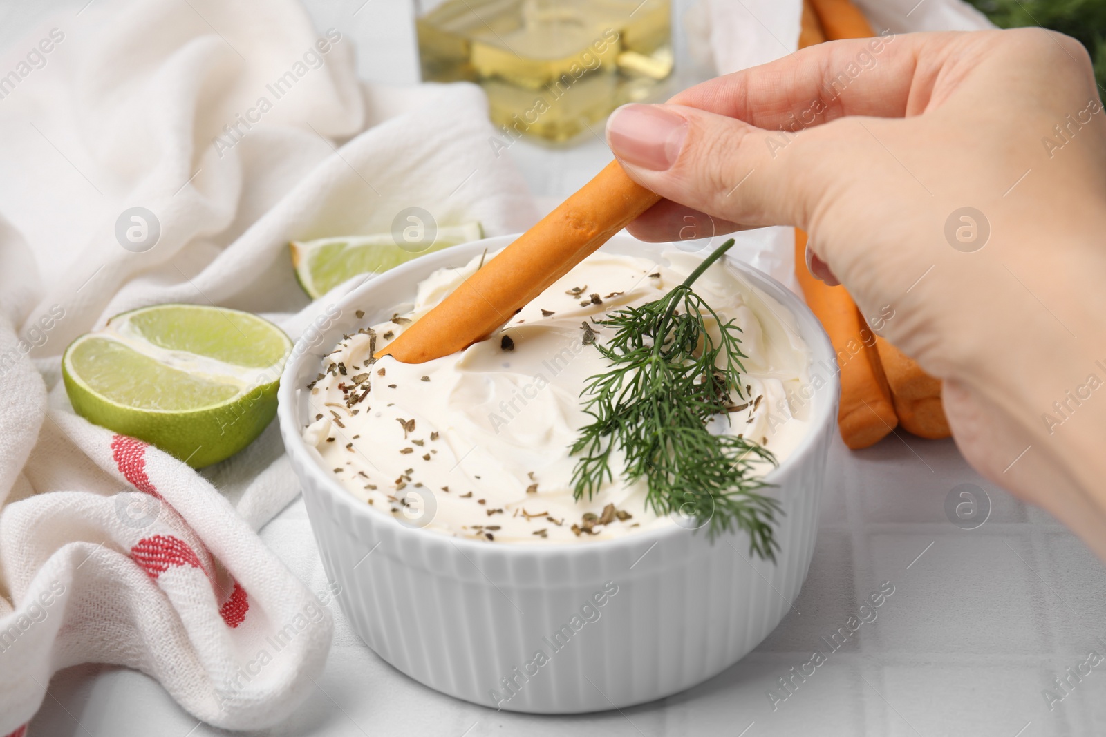 Photo of Woman dipping tasty grissini stick into cream cheese at white tiled table, closeup