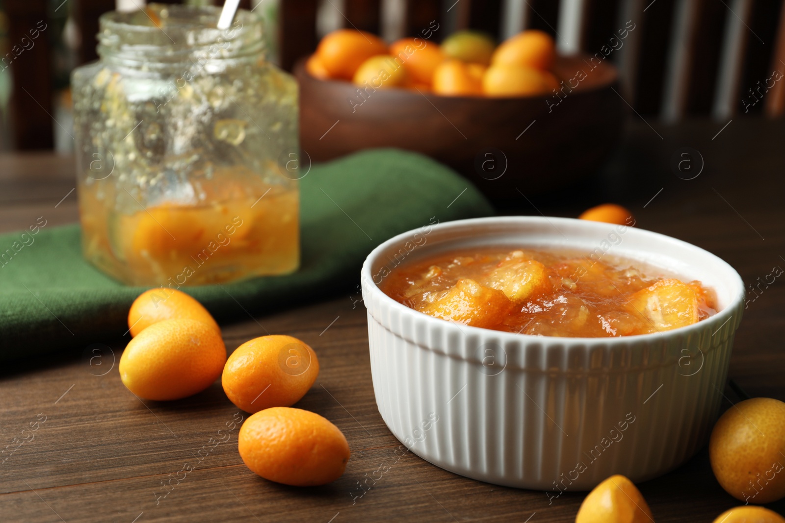 Photo of Delicious kumquat jam in bowl and fresh fruits on wooden table