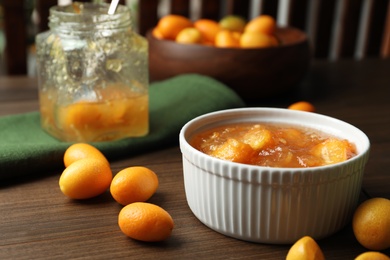 Delicious kumquat jam in bowl and fresh fruits on wooden table