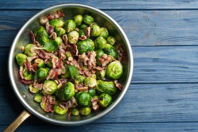 Photo of Delicious Brussels sprouts with bacon on blue wooden table, top view