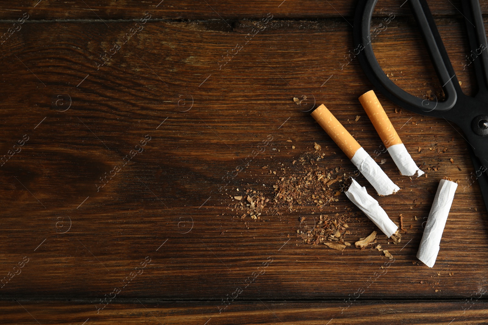 Photo of Cut cigarettes and scissors on wooden table, flat lay with space for text. Quitting smoking concept