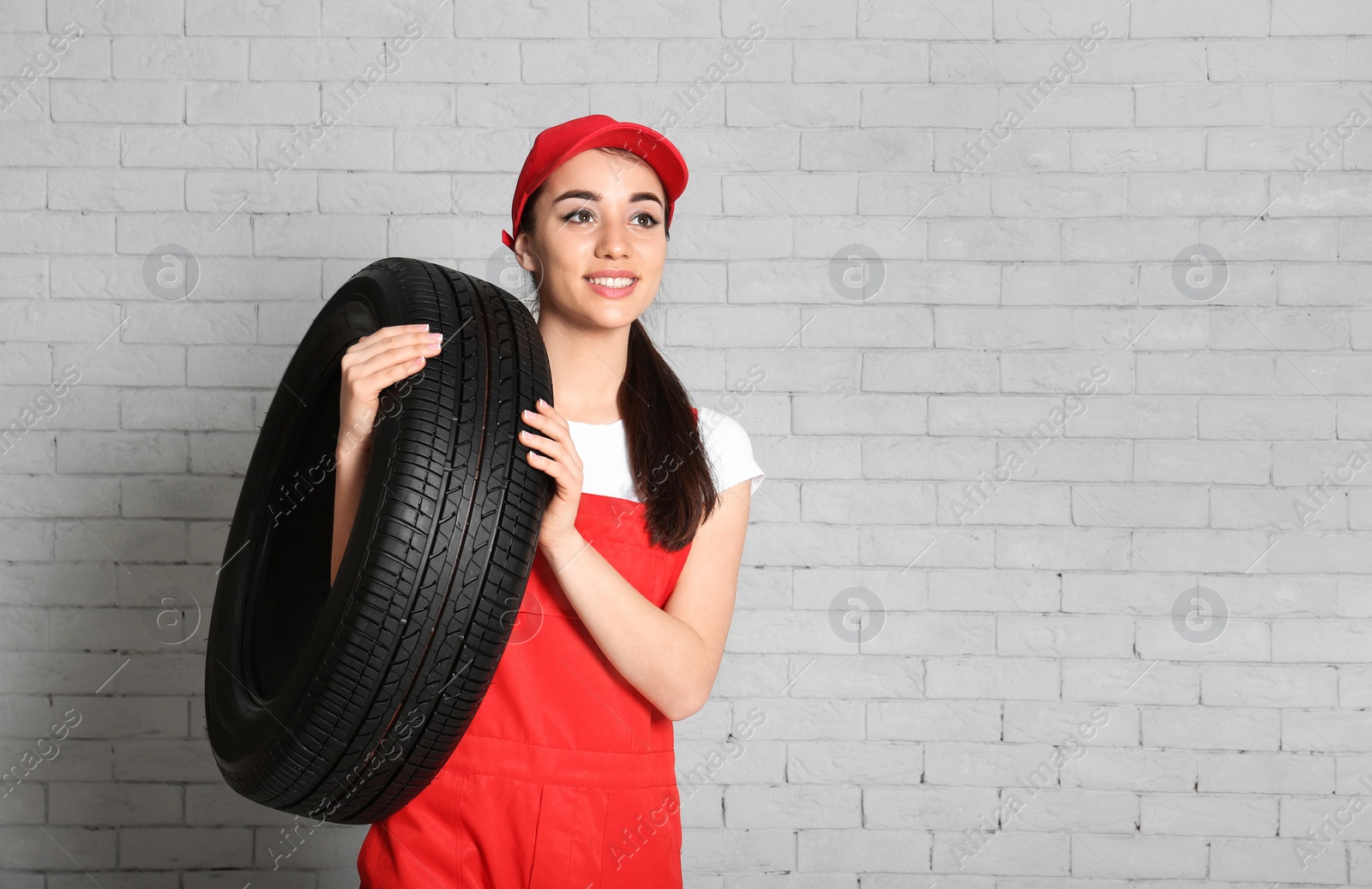 Photo of Female mechanic in uniform with car tire against brick wall background