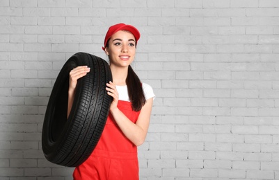 Female mechanic in uniform with car tire against brick wall background